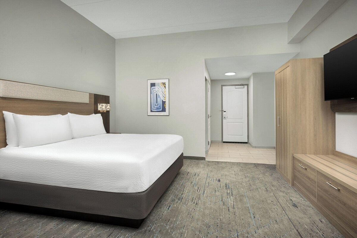 Quarto de hotel com uma cama grande, cabeceira de madeira, televisão de tela plana e um guarda-roupa.