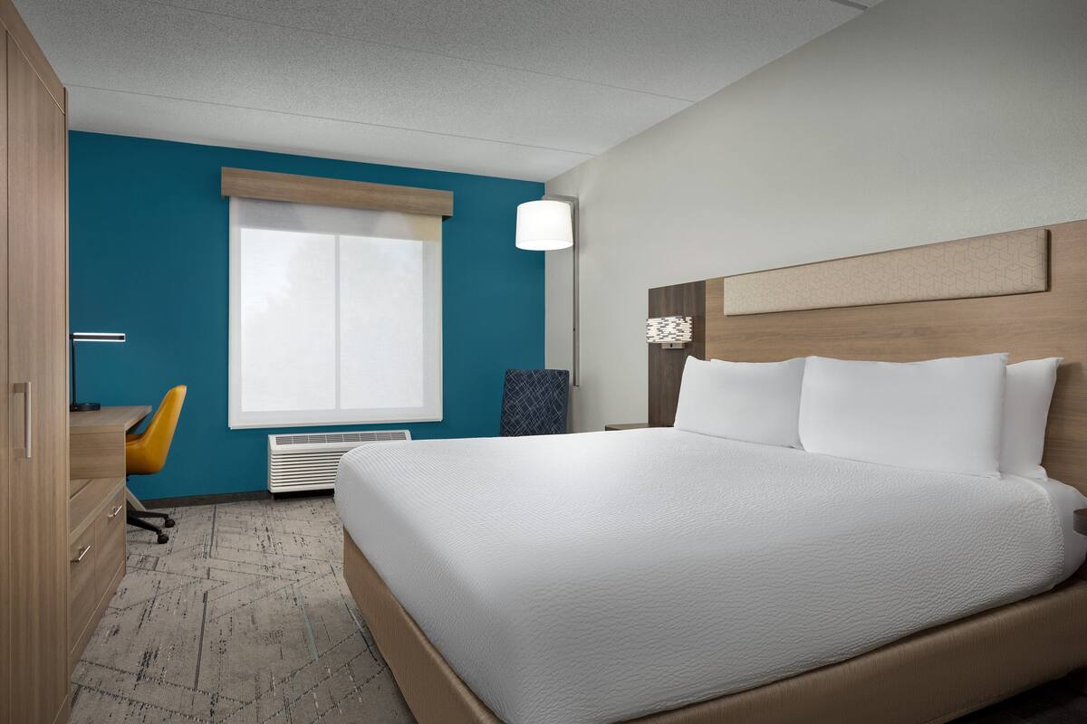 A modern hotel room with a large bed, a desk, and a chair.