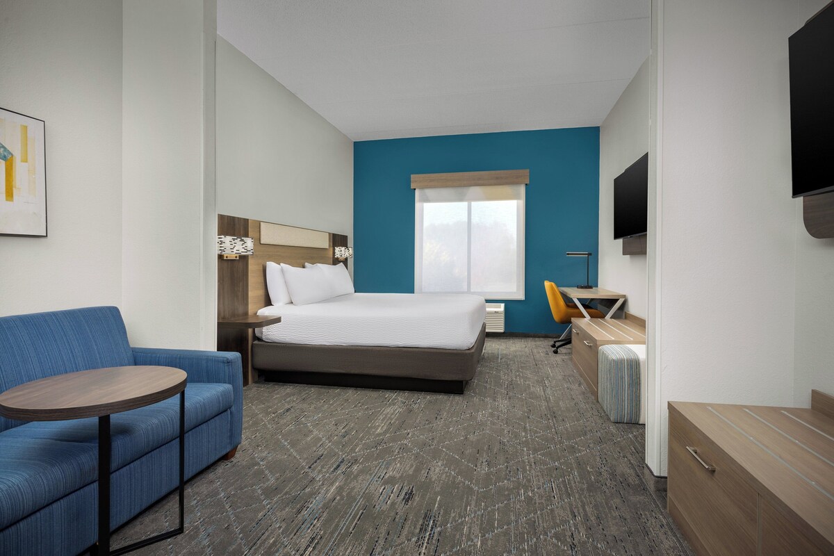 Quarto de hotel com cama, sofá, escrivaninha, cadeira e televisão.