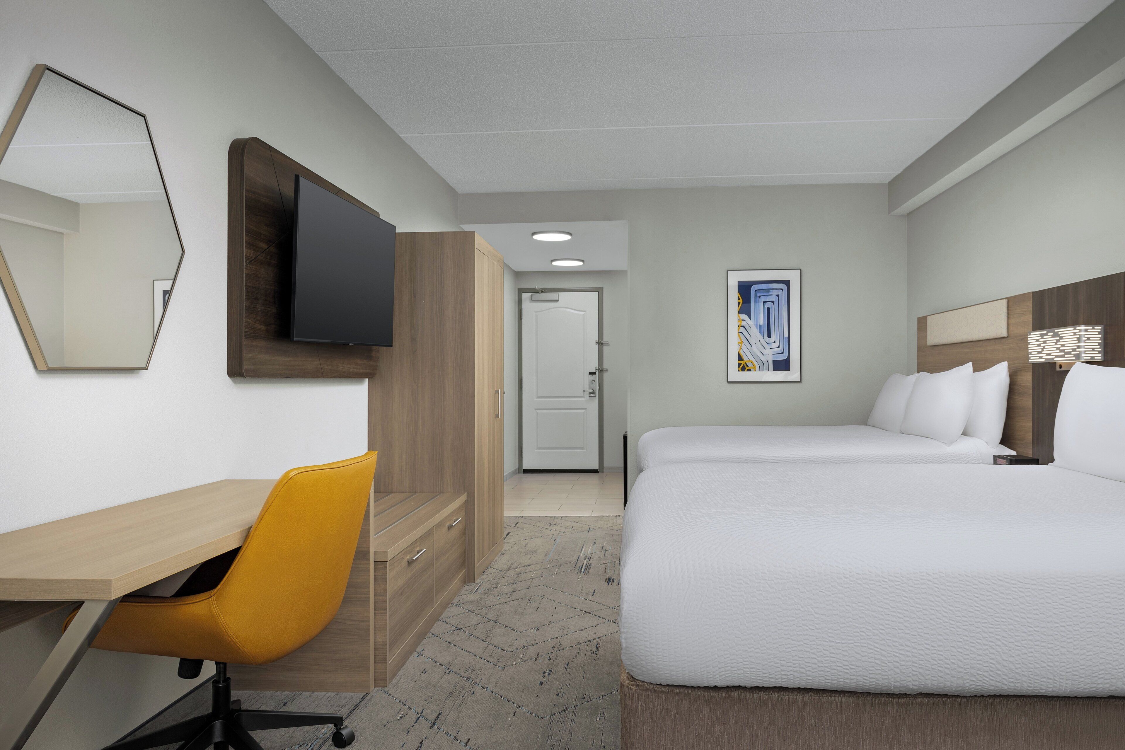 A hotel room with a bed, a desk, a chair, a television, and a door.