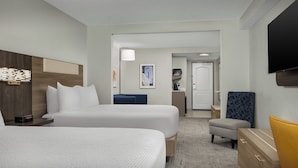 A hotel room with two beds, a desk, a chair, and a TV.
