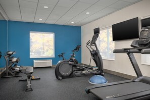 Un gimnasio con equipo de ejercicio, un ventanal grande y una televisión instalada.