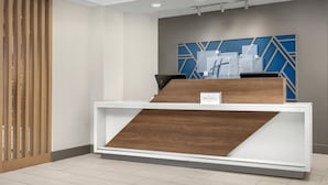 A reception desk with a modern design, a wooden accent panel, and a blue geometric wall art piece above it.