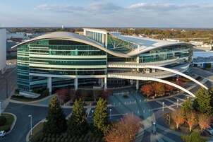 Un edificio moderno con arquitectura curvilínea, múltiples ventanales de vidrio y un estacionamiento con árboles.