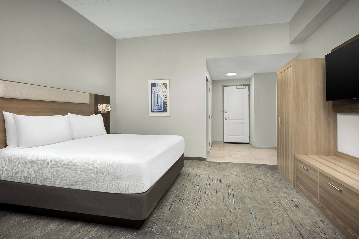 A hotel room with a large bed, a wooden headboard, a flat-screen TV, and a wardrobe.