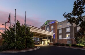 A hotel with a brick facade, a large entrance canopy, and flags. - Holiday Inn Express & Suites Greensboro Airport Area by IHG (Greensboro)