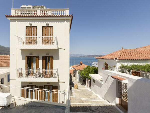 A two-story building with balconies, a clear view of the sea, and a hilly landscape in the background.