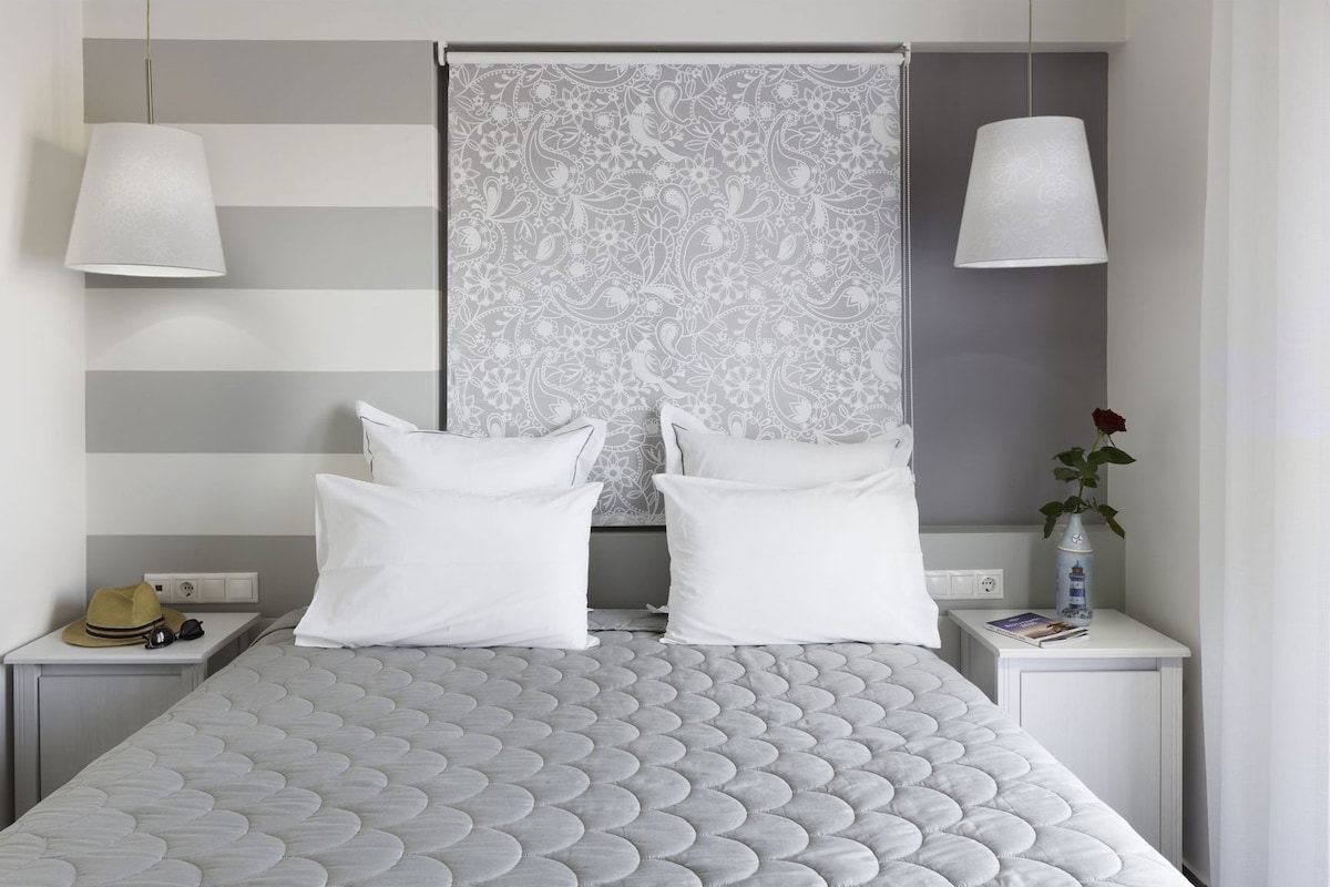 A neatly made bed with a patterned headboard, two bedside tables with lamps, and a vase with a rose on one table.