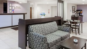 A modern hotel lobby with a reception desk, a sofa, a coffee station, and a dining area.
