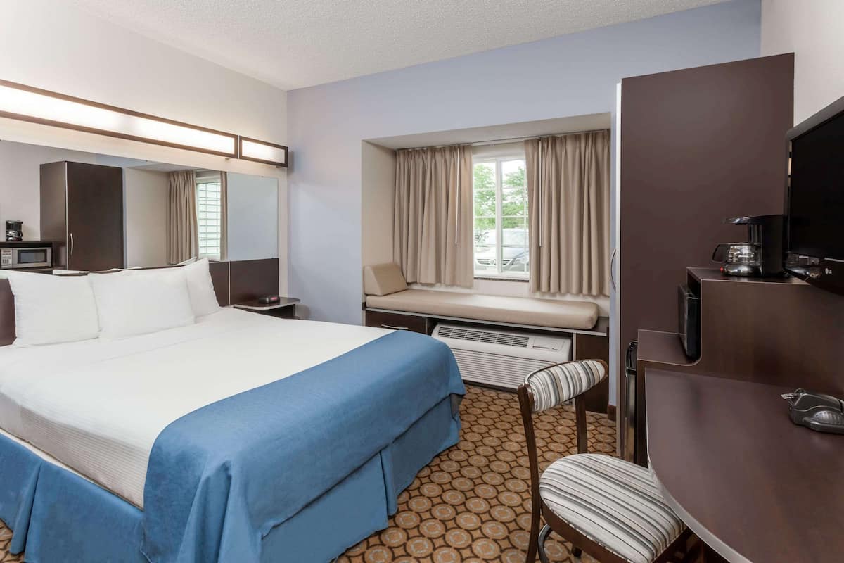 A hotel room with a large bed, a desk with a computer, a chair, a window with curtains, and a television.