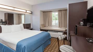 A hotel room with a large bed, a desk with a computer, a chair, a window with curtains, and a television.