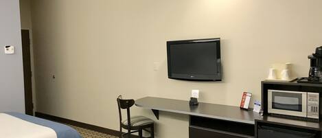 A hotel room with a bed, a desk with a chair, a television, a microwave, and a coffee maker.