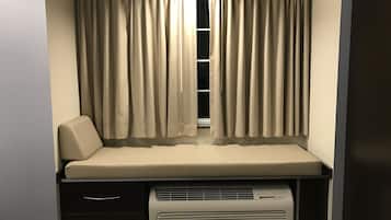 Een kleine kamer met raam, een bed, een tafeltje en een verwarming.