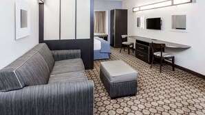 A hotel room with a sofa, a small table, a chair, a bed, a desk, and a TV.