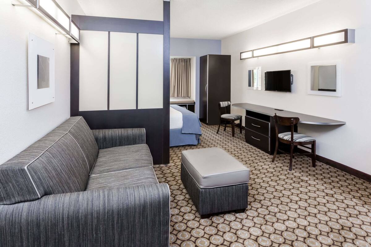 A hotel room with a sofa, a small table, a chair, a bed, a desk, and a TV.