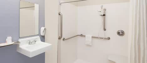 Une salle de bain équipée d’un lavabo, d’un miroir et d’une douche à l’italienne avec des barres d’appui.