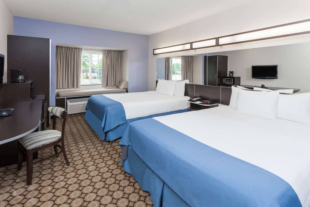 A hotel room with two beds, a desk with a chair, a TV, and a microwave.