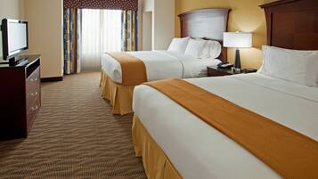 A hotel room with two beds, a television, a desk with a lamp, and a window with curtains.