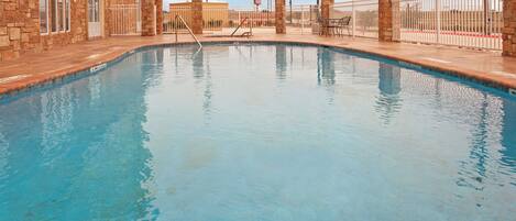 A swimming pool with a stone wall on one side and a metal fence on the other.