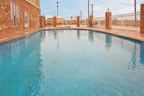 A swimming pool with a stone wall on one side and a metal fence on the other.