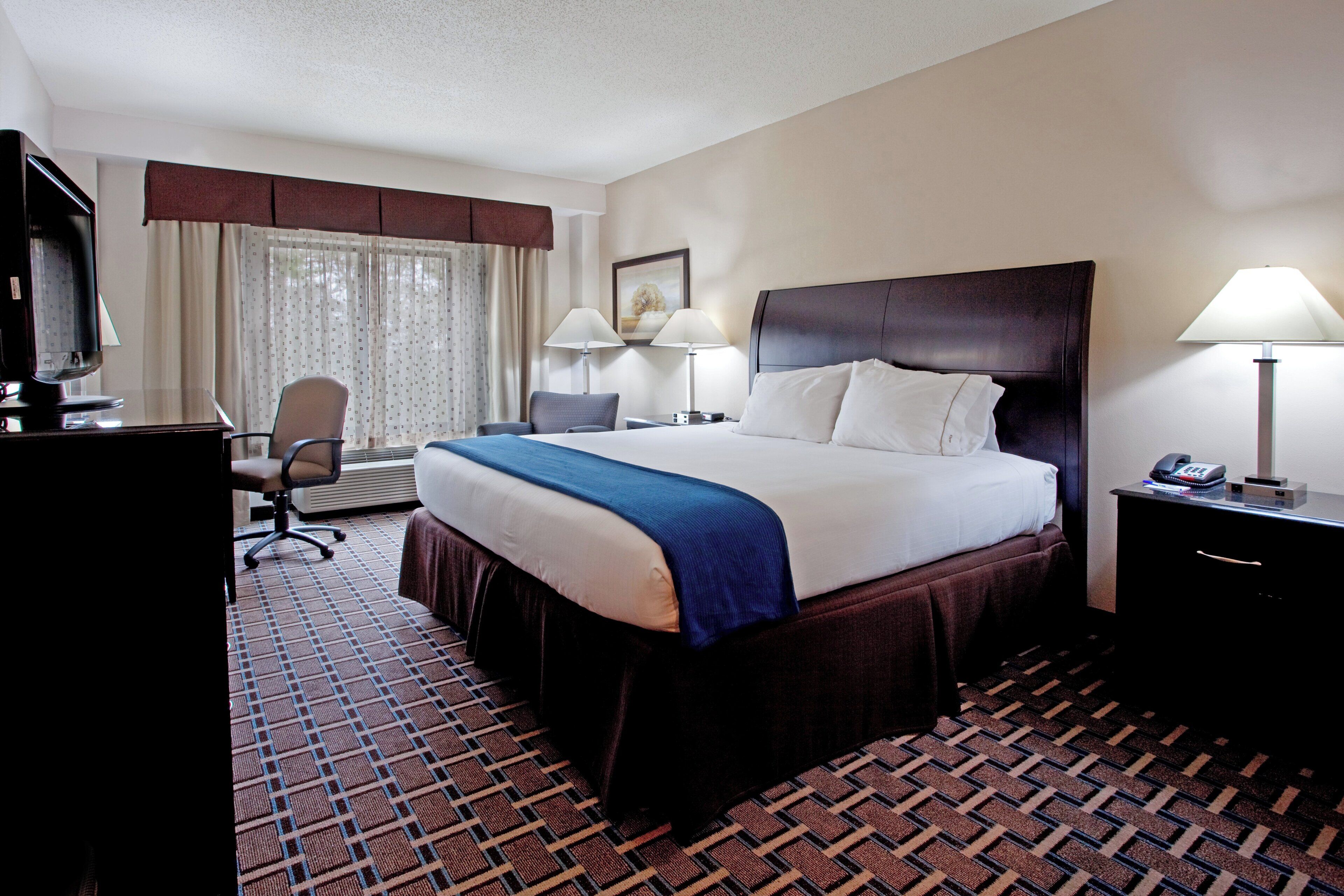A hotel room with a bed, desk, chair, and a television.
