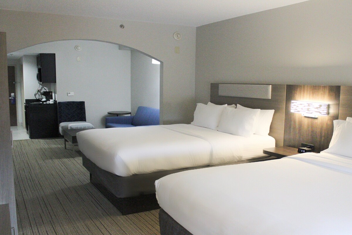 A hotel room with two beds, a desk, a chair, and a TV.