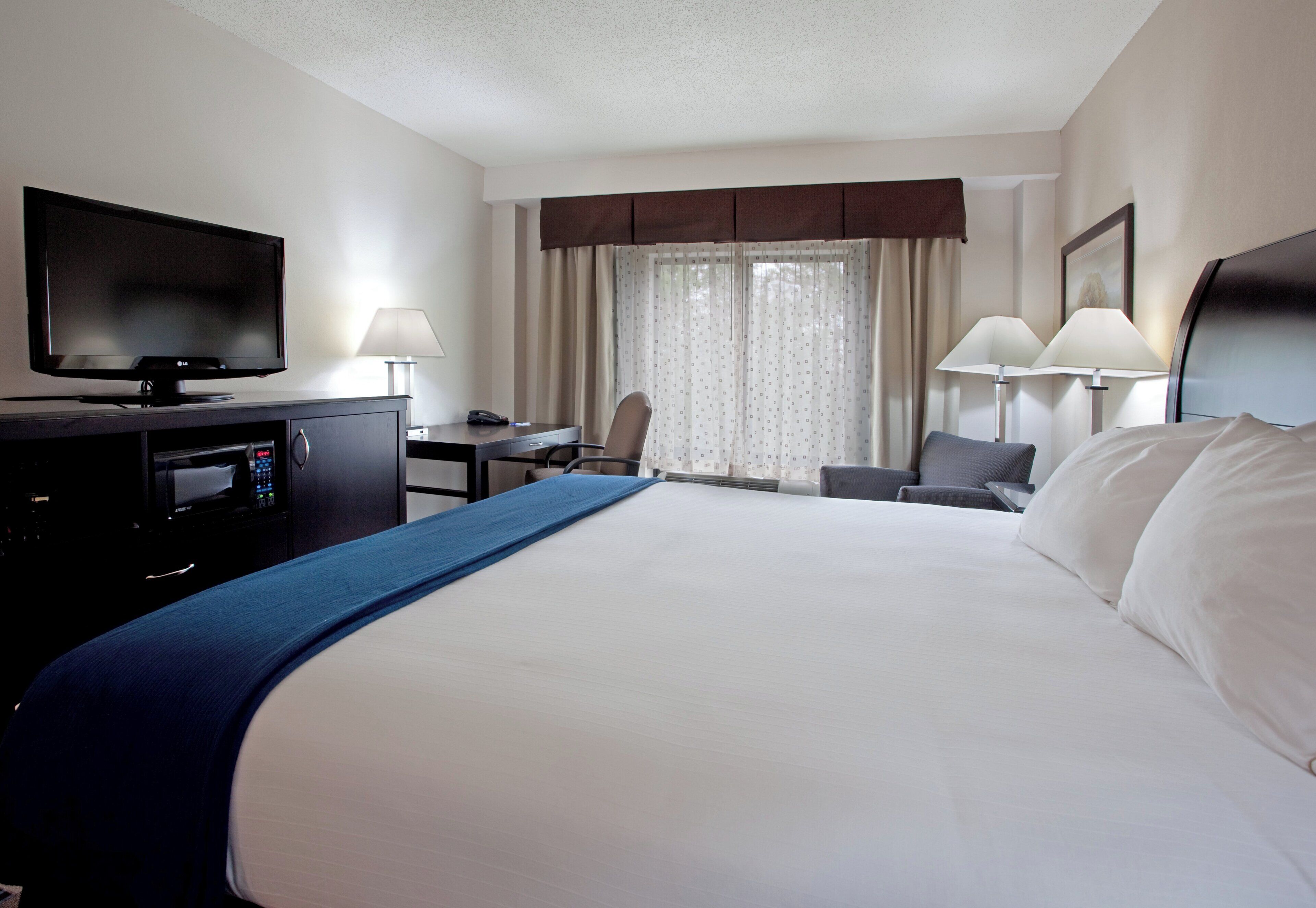 Una habitación de hotel con una cama grande, un escritorio con computadora, un televisor y dos lámparas.