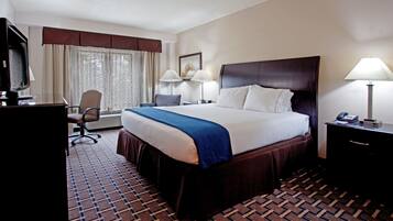 A hotel room with a large bed, two bedside lamps, a desk with a computer, a chair, and a TV.