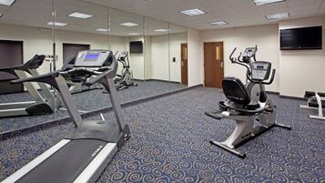 Un gimnasio equipado con cintas de correr, bicicletas estáticas y un espejo grande.