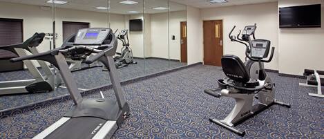 Un gimnasio equipado con cintas de correr, bicicletas estáticas y un espejo grande.