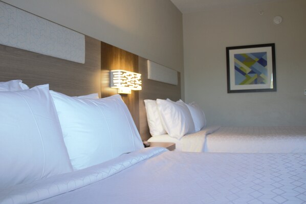 A hotel room with two beds, a headboard with a light fixture, and a framed abstract art piece on the wall.