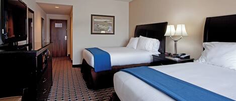A hotel room with two beds, a television, a desk with a lamp, and a framed picture on the wall.