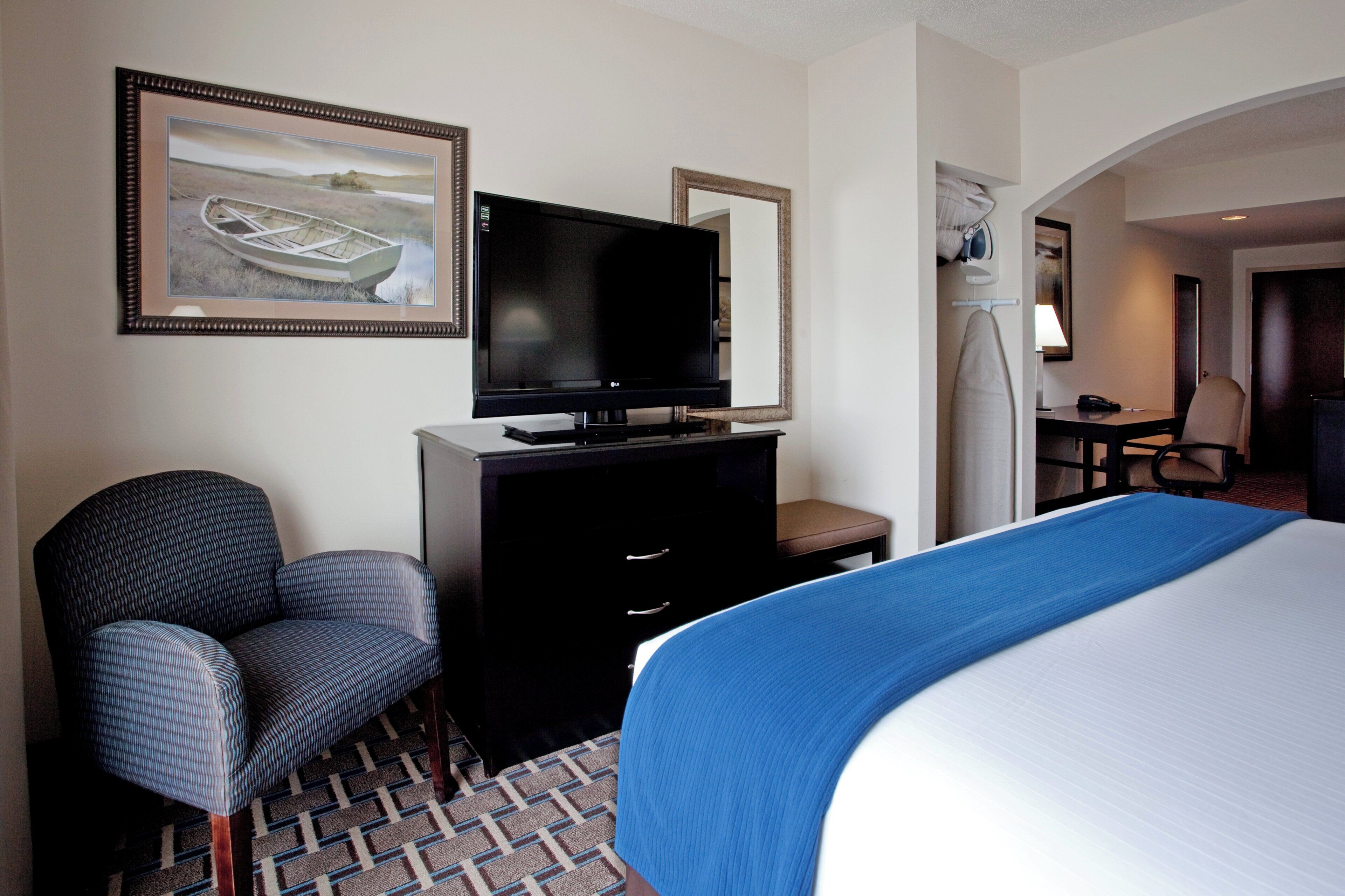 Una habitación de hotel con una cama, un televisor en una cómoda, una silla y un escritorio con una lámpara.