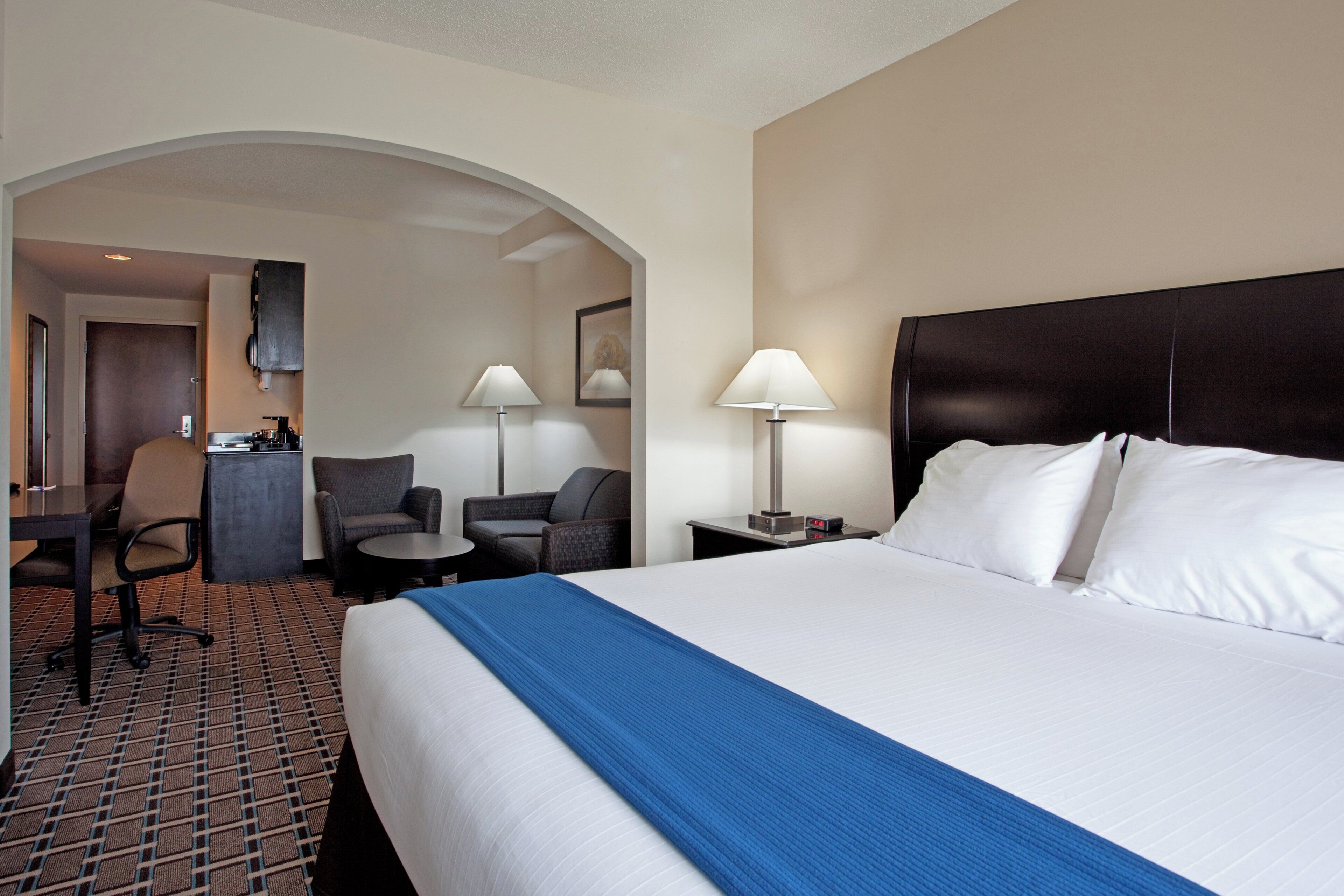 A hotel room with a large bed, two chairs, a desk, and a small table.
