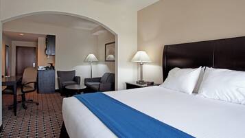 A hotel room with a large bed, two chairs, a desk, and a small table.