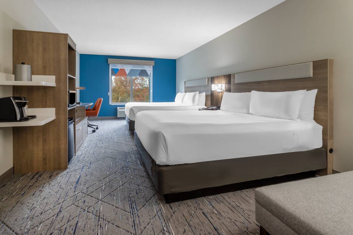 A hotel room with two beds, a desk, a chair, and a large window.