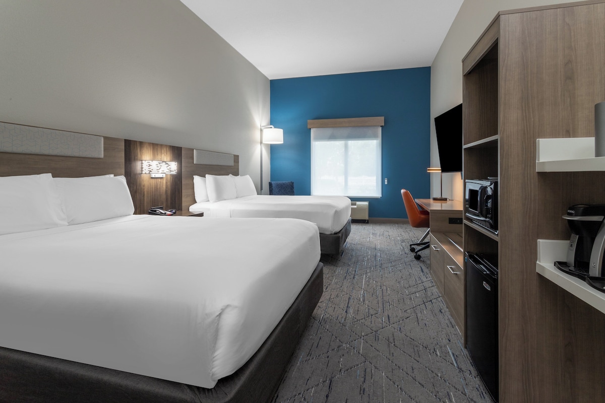 A hotel room with two beds, a desk, a microwave, and a TV.