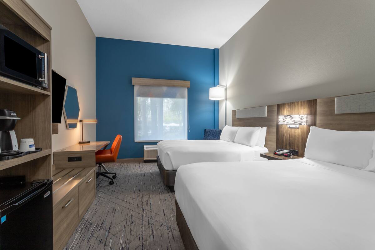 A hotel room with two beds, a desk with a chair, a television, and a window with curtains.