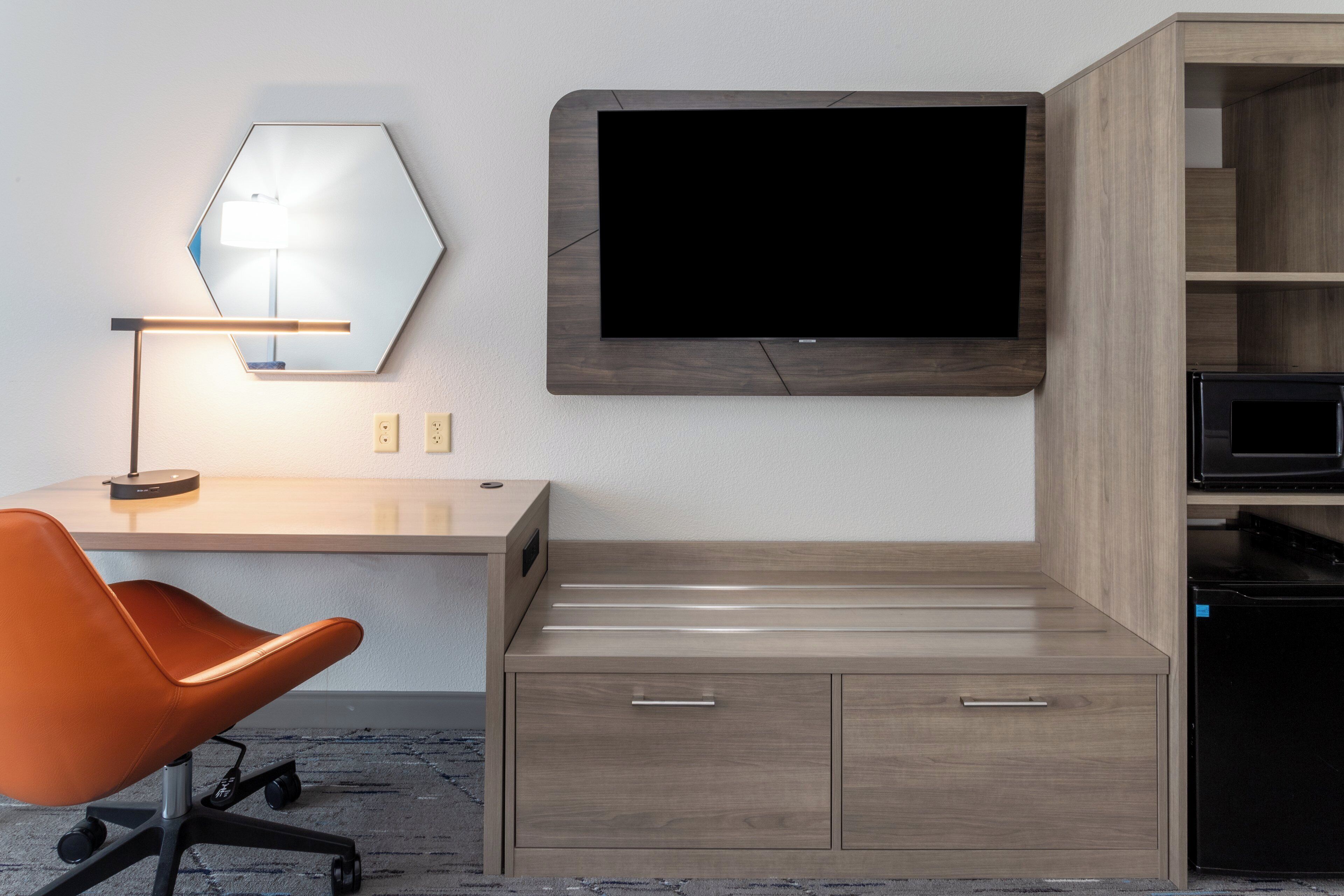 A hotel room with a desk, chair, television, and built-in microwave.