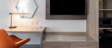 A hotel room with a desk, chair, television, and built-in microwave.
