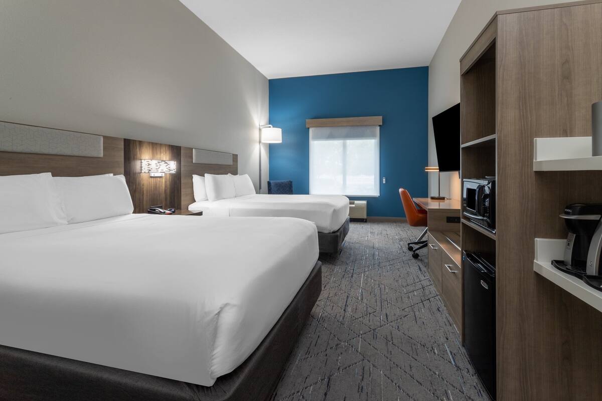 A hotel room with two beds, a desk, a microwave, and a TV.
