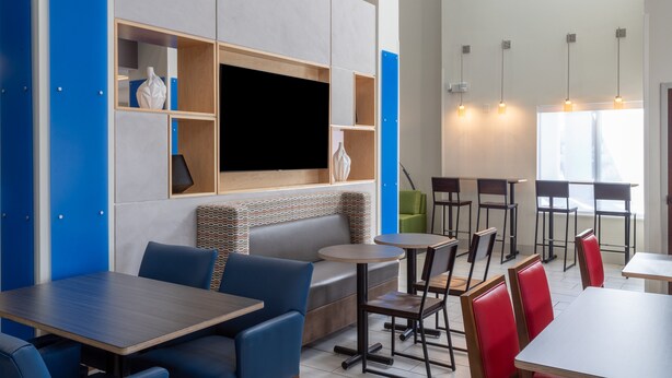 A modern restaurant with high ceilings, blue and grey walls, and a variety of seating options including tables, booths, and chairs. - Holiday Inn Express Crystal River by IHG (Crystal River)
