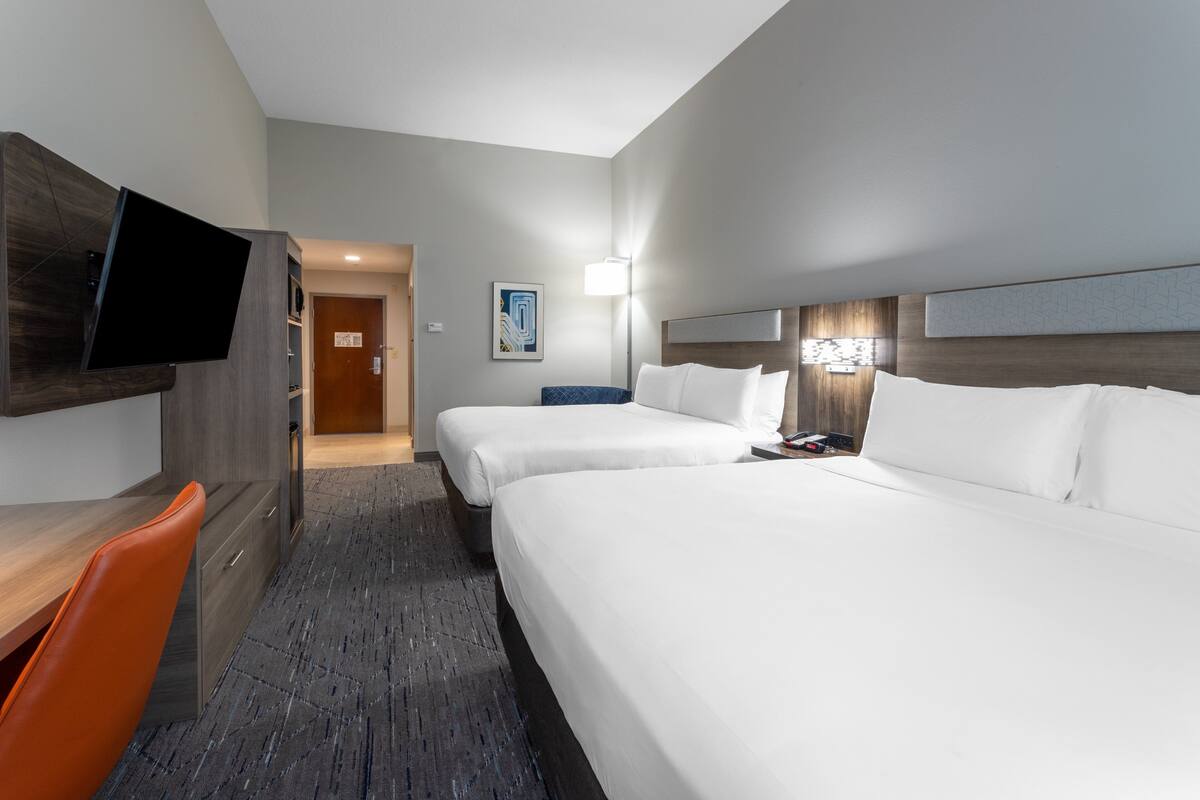 A hotel room with a desk, two beds, a TV, and a painting on the wall.