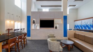 A modern hotel lobby with a long dining table, several chairs, a sofa, a small round table, and a large flat-screen TV mounted on the wall. - Holiday Inn Express Crystal River by IHG (Crystal River)