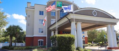 Edificio de Holiday Inn Express con entrada cubierta, palmeras y estacionamiento.