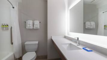 Un baño con inodoro blanco, lavabo con espejo y zona de ducha.