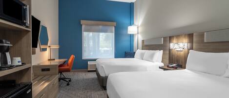 Habitación de hotel con dos camas, un escritorio con silla, televisor y ventana con cortinas.
