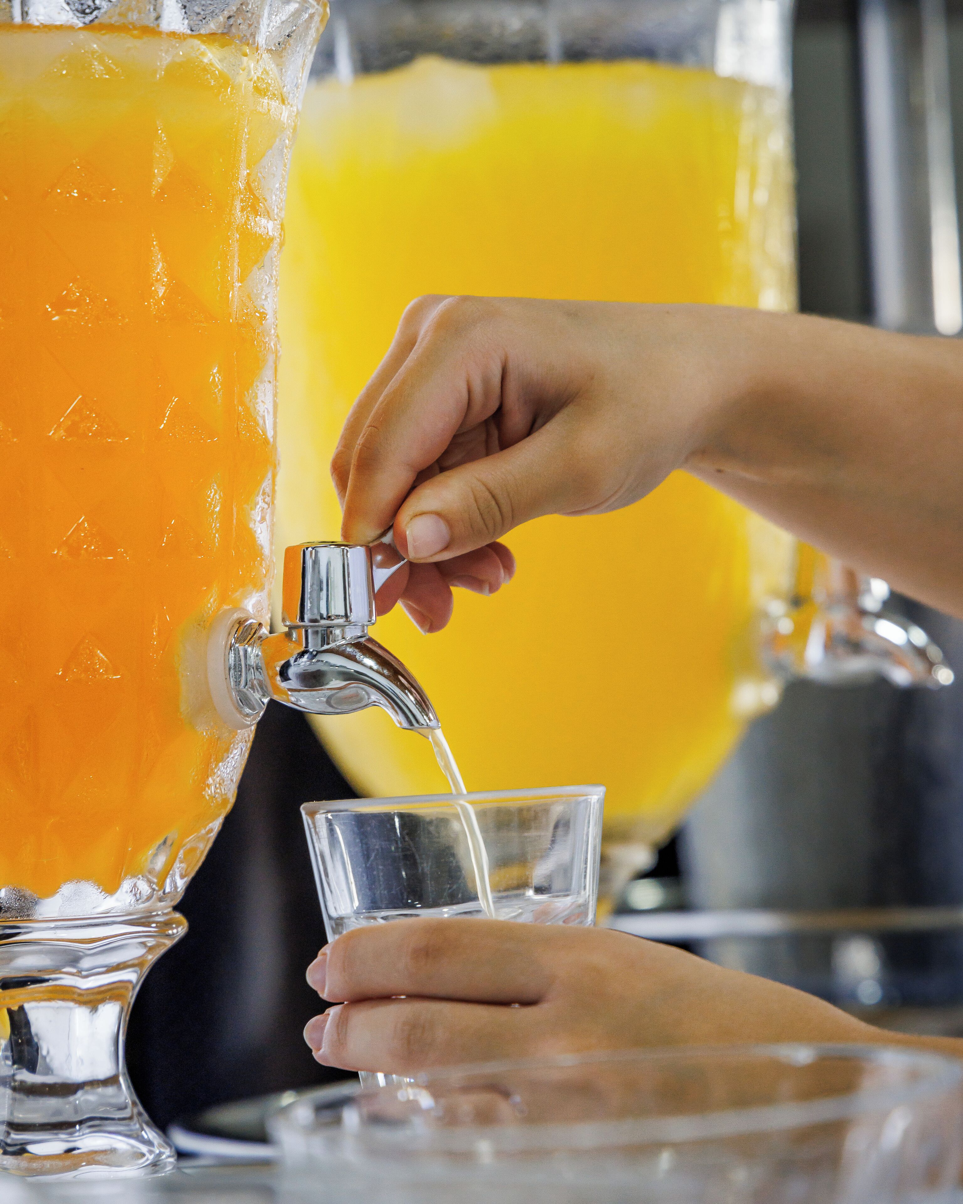 A hand pouring orange juice from a large pitcher into a glass.