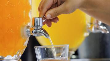 A hand pouring orange juice from a large pitcher into a glass.