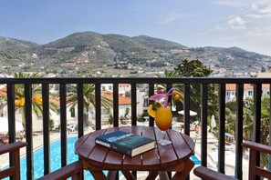 Una mesa de madera con un libro y una bebida en un balcón con vistas a una piscina y montañas.